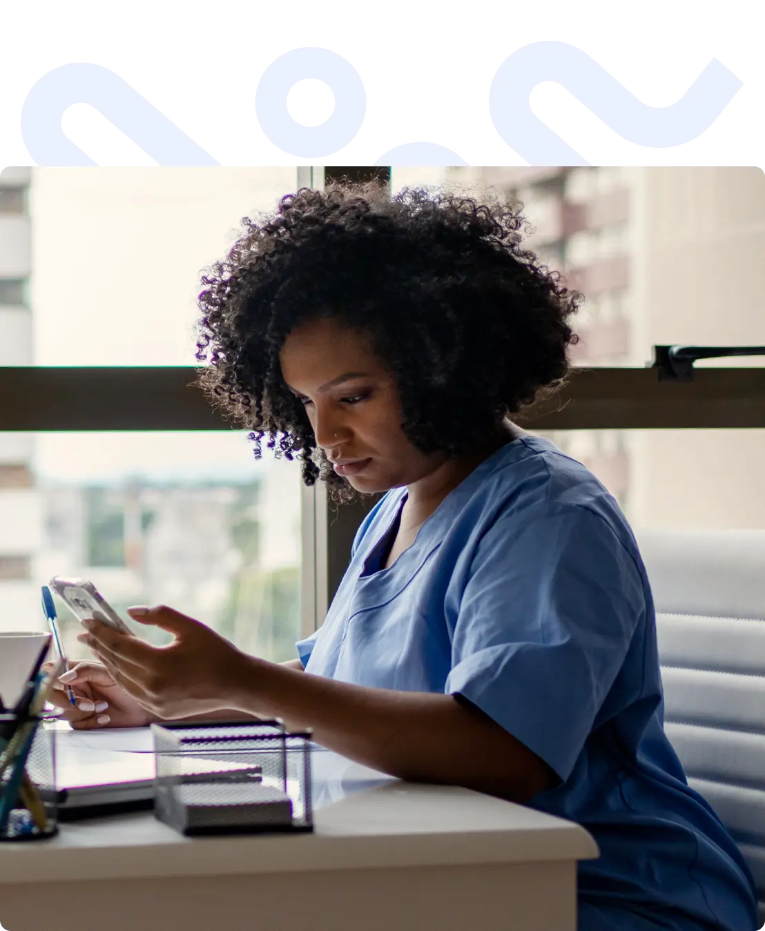 Doctor at her desk looking at her phone, with a pen in hand ready to write down results.